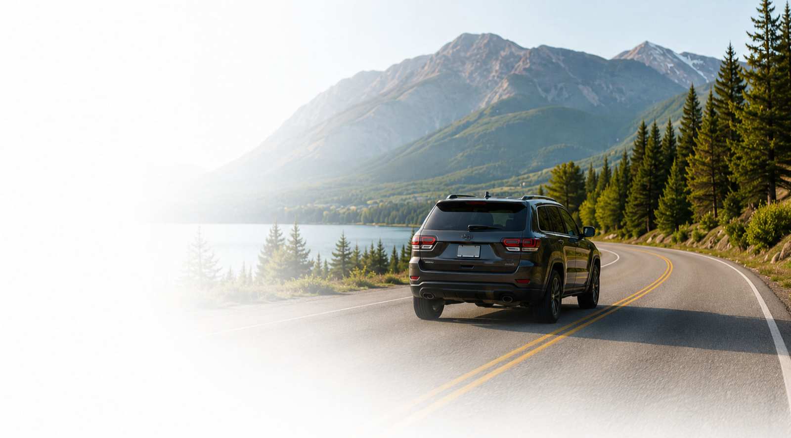 SUV driving a winding mountain road beside a lake
